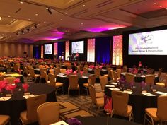 a room filled with lots of tables covered in black tablecloths and purple flowers