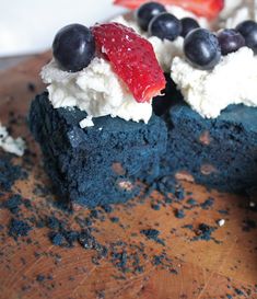 a piece of cake with blueberries and strawberries on top is sitting on a cutting board