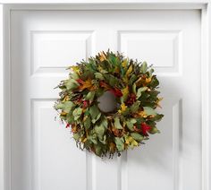 a wreath hanging on the front door of a white house with red and yellow flowers