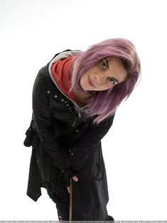 a woman with pink hair and black jacket posing for the camera in front of a white background