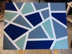 a blue and white abstract painting sitting on top of a wooden easel in a room