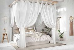 a bed with white drapes hanging from it's sides and pillows on the floor