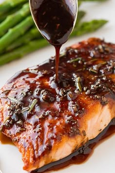 a piece of salmon covered in bbq sauce being drizzled over asparagus