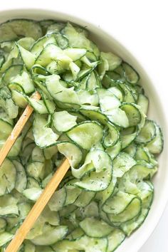 cucumber salad in a white bowl with wooden spoons