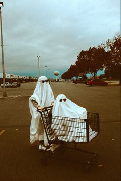 a person in a white robe pushing a shopping cart with two bags on top of it