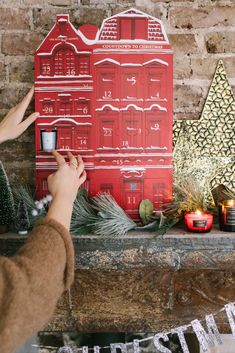 someone decorating a red christmas card on a mantel with candles and greenery