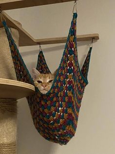 a cat sitting in a crocheted hammock hanging from a shelf