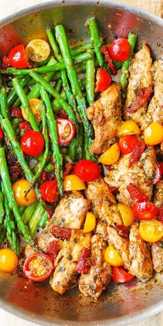 a pan filled with chicken, asparagus and tomatoes