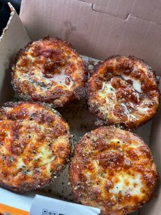 four small pizzas in a box with cheese and sauce on them, ready to be eaten