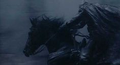 a man riding on the back of a black horse in the rain at night with it's head down