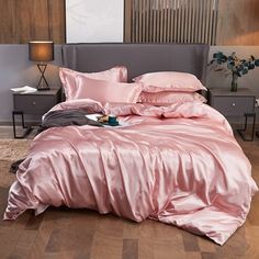 a bed with pink sheets and pillows on top of it in front of a wooden floor