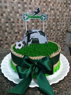 a cake decorated with grass and soccer balls is on a plate that has a green bow around it