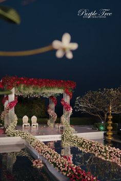 an outdoor wedding setup with flowers and greenery on the ground at night, lit up by lights