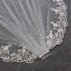 a white lace and beaded veil with pearls on it's edge sits on a gray surface