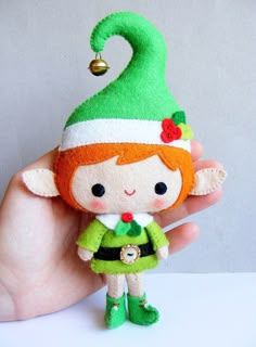 a hand holding a small elf doll in it's right hand with a bell on its head