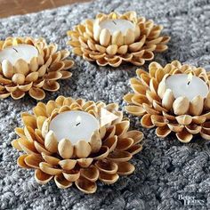 three candles are sitting on top of a gray blanket with pine cones around them and one candle is lit