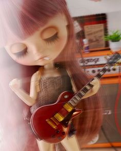 a doll with long hair holding a red guitar