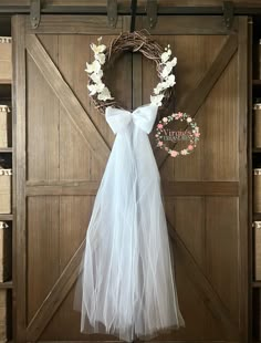 a white wedding dress hanging on a barn door with a wreath and flowers in it