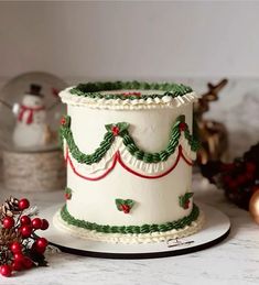 a white cake decorated with green and red decorations on top of a table next to ornaments