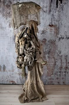 a statue made out of cloth and other items on top of a wooden floor next to a wall