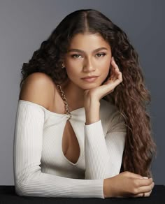 a beautiful young woman sitting at a table with her hand on her chin and looking off to the side