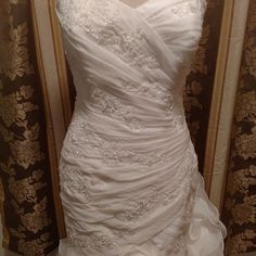 a white wedding dress is on display in front of a gold and black wallpaper