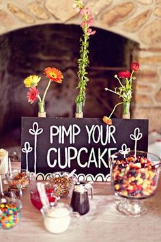 a table topped with lots of candies and flowers next to a sign that says pimp your cupcake