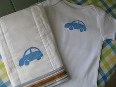 two baby onesuits with blue cars on them sitting next to a plaid tablecloth