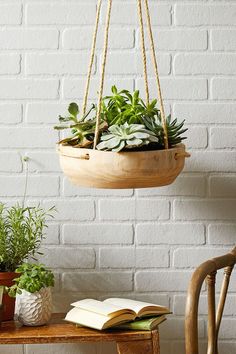 a hanging planter filled with green plants next to a book on a wooden table