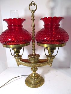 two red glass vases sitting on top of a metal stand with one light on it