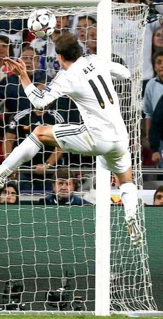 a soccer player jumping up to catch the ball in front of him and people watching