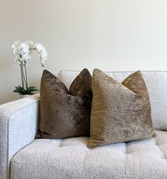 two pillows sitting on top of a couch next to a vase with flowers in it