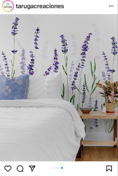 a bed with white sheets and purple flowers painted on the wall behind it, along with a small wooden table