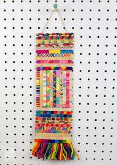 a wall hanging made out of different colored paper strips and tassels on a pegboard