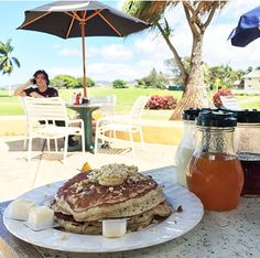 pancakes on a plate with syrup and honey in front of an outdoor dining area at a resort