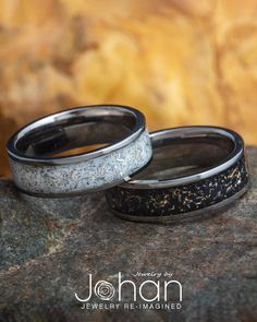 two wedding bands with black and white speckles on them sitting on top of a rock