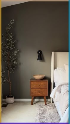 a bed room with a neatly made bed and a night stand next to a potted plant