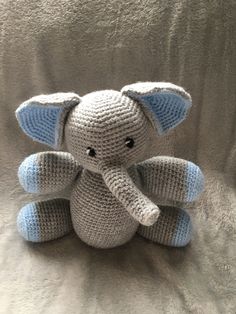 a crocheted stuffed elephant sitting on top of a white bed sheet with its trunk in the shape of an elephant