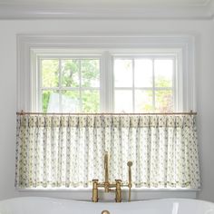 a bath tub sitting under a window next to a white sink and counter top with a faucet