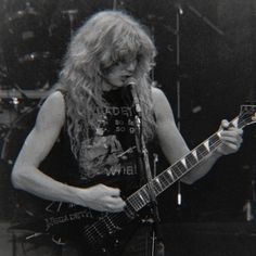 a man with long hair holding a guitar in front of a microphone and playing the guitar