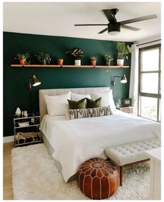 a bedroom with dark green walls and white bedding, potted plants on the wall