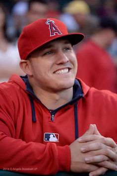 a baseball player wearing a red hat and sitting in the dugout with his arms crossed