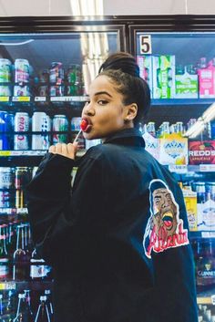 a woman standing in front of a store filled with drinks and sodas while brushing her teeth