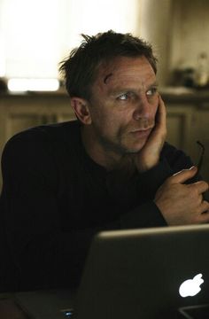 a man sitting in front of a laptop computer with his hand on his chin looking at the screen