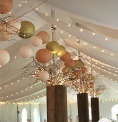 a room filled with lots of lights and tall vases full of branches covered in paper lanterns