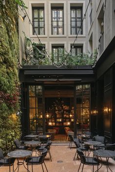 tables and chairs in front of a building with plants growing on the outside wall above them