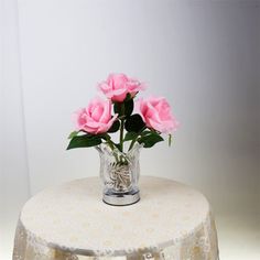 three pink roses in a clear vase on a white table cloth with lace doily