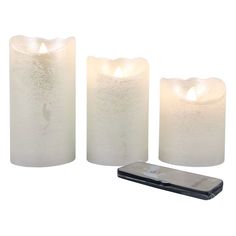 three white candles sitting next to a cell phone