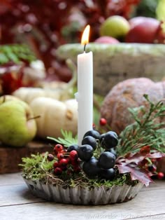 a white candle sitting on top of a wooden table next to fruit and veggies