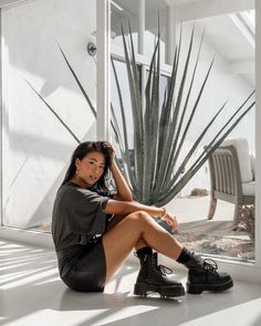 a woman sitting on the floor next to a cactus in front of a glass window